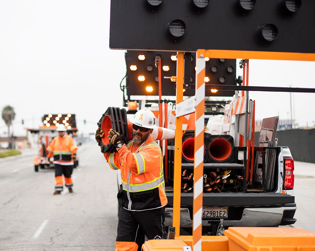 man in sunglasses carrying traffic cones on shoulder