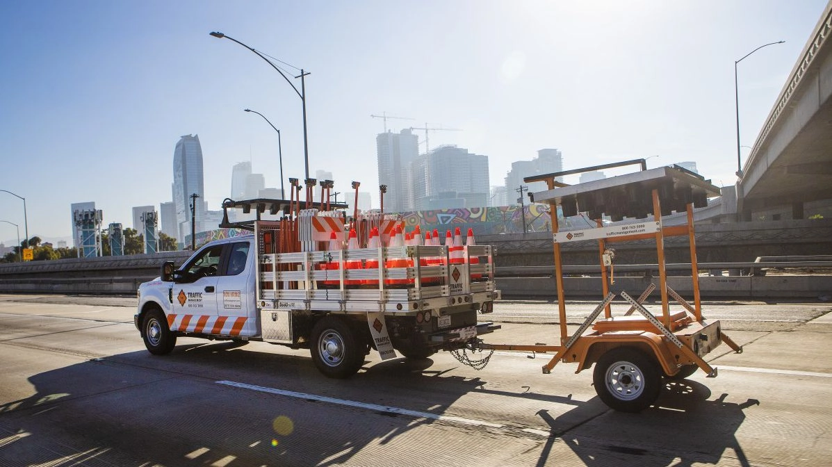 white Traffic Management Inc truck carrying traffic cones and hauling lights on city freeway