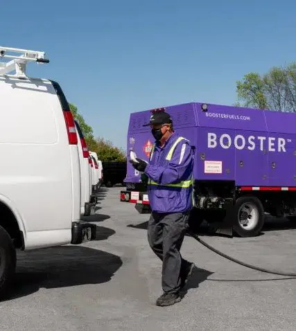 masked Booster fueling professional dragging hose to white van