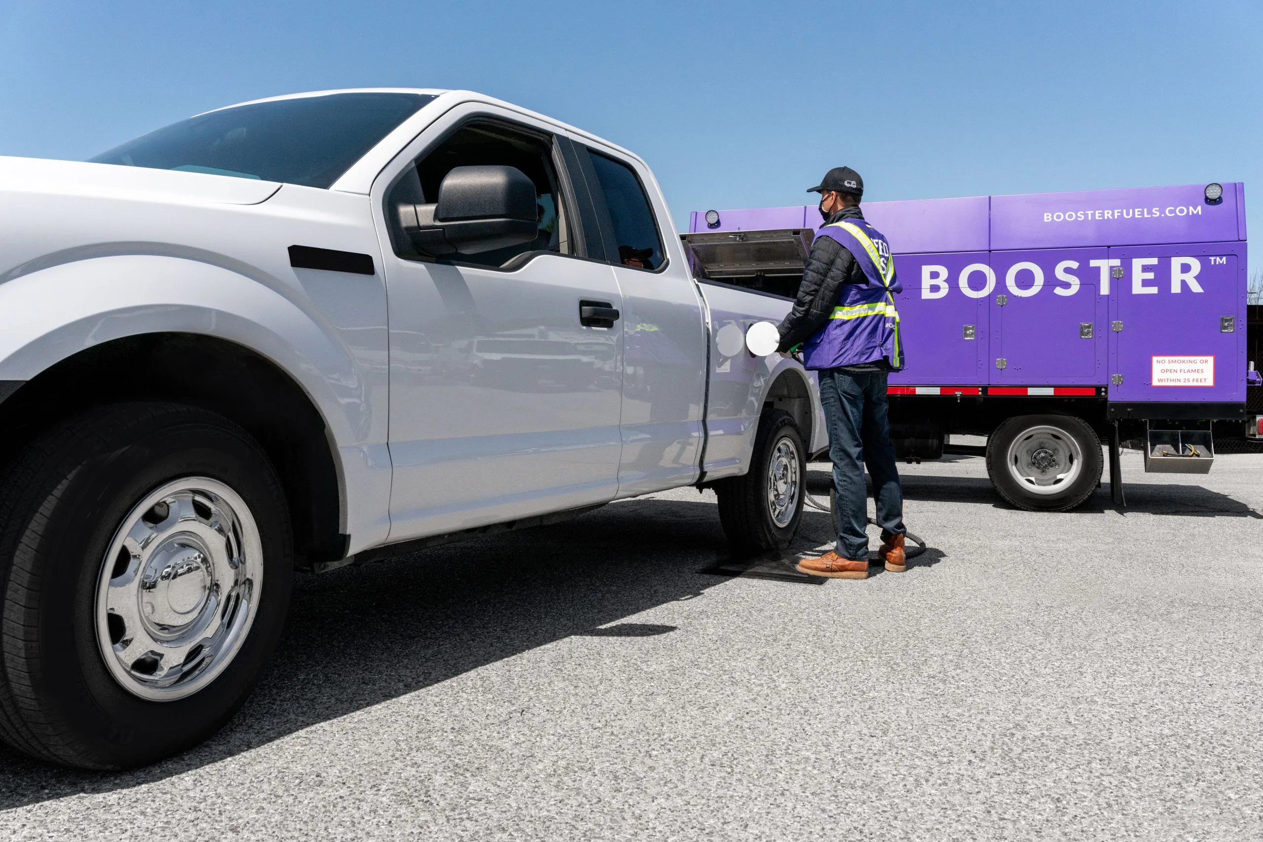 man in mask wet hose fueling a white truck from a Booster truck