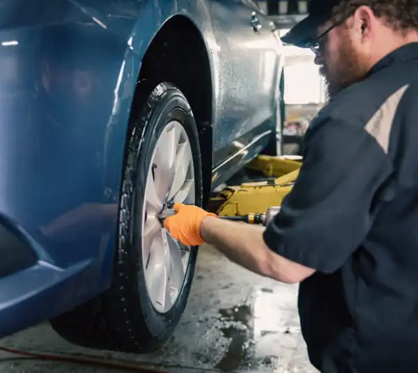 mechanic changing tire on blue car